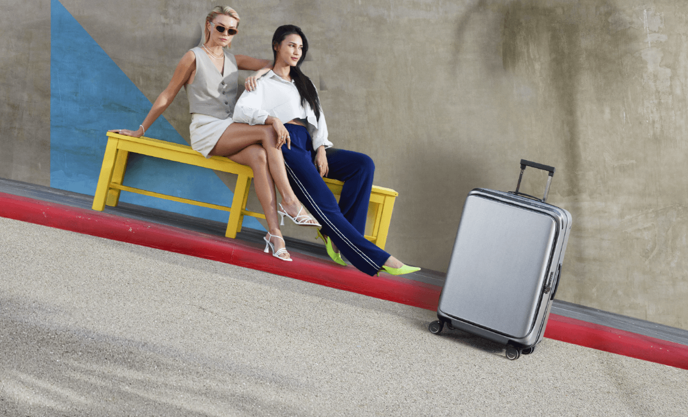 Unimax luggage with two female models sitting down on a yellow bench in the background